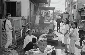 Prints of Vietnamese children beside food stalls, one of the stallholders wearing a traditional non la hat, in Saigon, Vietnam, 30th August 1965 Vietnam Prints: Life In Saigon
