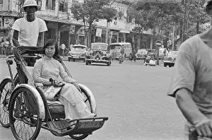 Prints of A cycle rickshaw, the driver wearing a safari-style hat, transports a young Vietnamese woman through the streets of Saigon, Vietnam, 30th August 1965 Vietnam Prints: Life In Saigon