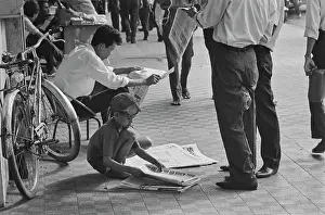 Prints of A young Vietnamese boy folding newspapers for sale on a street in Saigon, Vietnam, 30th August 1965 Vietnam Prints: Life In Saigon