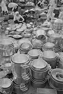 Prints of Vietnamese women, some wearing traditional non la hats, sit beyond a collection of pots and pans for sale on a street in Saigon, Vietnam, 30th August 1965 Vietnam Prints: Life In Saigon