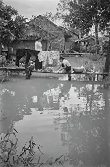 Prints of Two Vietnamese women stand on a narrow footbridge as they wash clothes, some of which are hanging on a clothesline, in Saigon, Vietnam, 30th August 1965 Vietnam Prints: Life In Saigon