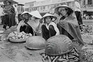 Prints of Vietnamese women, wearing traditional non la hats, shelter themselves from the rain with shawls, selling vegetables on an embankment of the Saigon River as it flows through Saigon, Vietnam Vietnam Prints: Life Along The Saigon River