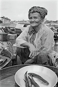 Prints of An elderly Vietnamese woman wearing a headscarf sits beside a bowl of fish on an embankment of the Saigon River in Saigon, Vietnam, 30th August 1965 Vietnam Prints: Life Along The Saigon River