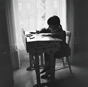 Studying Prints: Little girl silhouetted at window, sitting at desk, studying, urban view out of window