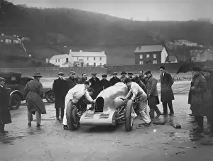 Prints of 3rd January 1927: People from the local town watch a group of mechanics inspect Captain Malcolm Campbells racing car Bluebird during his attempt to break the land speed record at Pendine Sands Topical Press Agency Prints: Local Curiosity