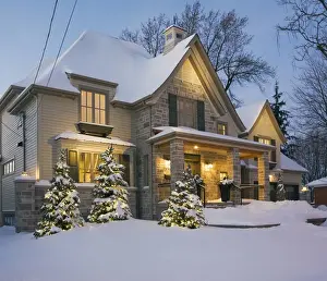 Luxurious residential cottage style home with illuminated evergreen trees at dusk in winter, Quebec, Canada