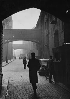 A man in a bowler hat walking under the arches on the cobbled Wapping High Street, London