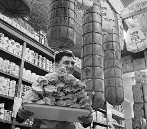 Groceries Prints: Man Carrying Hero Sandwiches Below Large Cheeses