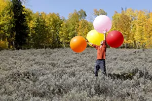 Man carrying huge balloons, landscape in fall, Utah, USA