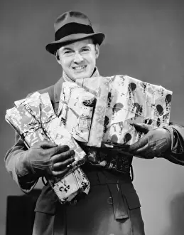 Man with coat, gloves and hat carrying Christmas gifts