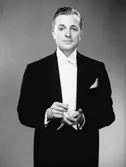 Man in dinner jacket holding cigarette and cigarette case standing in studio, (B&W), portrait
