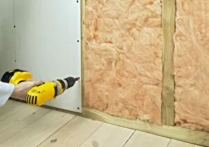 Man drilling screws in plasterboard and batten to hide insulation, close-up