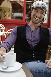 Spare Prints: Man, early 30s, wearing casual clothes sitting in an outdoor cafAzA with a coffee cup