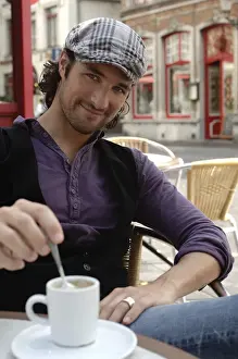 Spare Prints: Man, early 30s, wearing casual clothes sitting in an outdoor cafAzA stirring a coffee cup