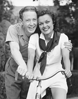Man embracing woman sitting on bike, (B&W), portrait