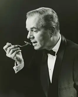 Biting Prints: Man holding fork, taking bite in studio, (B&W), portrait