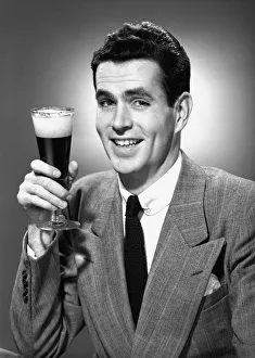 35 39 Years Gallery: Man holding glass of beer in studio, (B&W), portrait