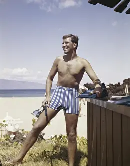 1963 Prints: Man holding snorkel and flippers on beach, smiling