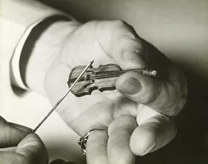 Retrofile Gallery: Man holding tiny violin, close up of hands