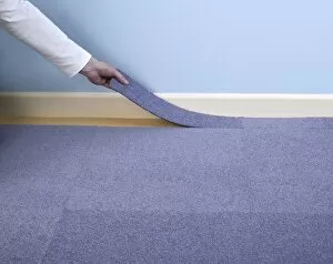 Man installing blue carpet tile next to skirting board