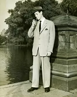 Man lighting cigarette by lake in park, (B&W)
