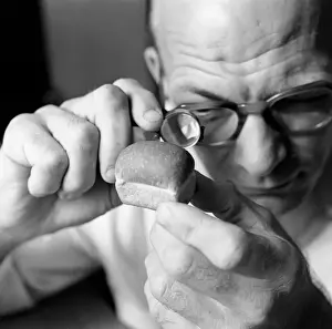 Man looking at miniture loaf of bread through magnifying glass