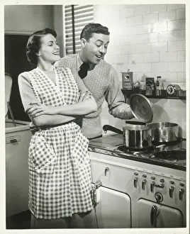 Man looking into pot in domestic kitchen, woman smiling