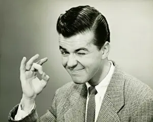 Man making OK gesture, winking in studio, (B&W), portrait