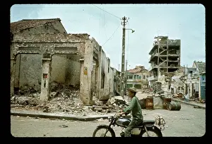 Man on Moped Rides Past Bombed Building