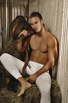 Serious Prints: Man with a naked torso wearing long underwear in a horse barn sitting on bales of hay