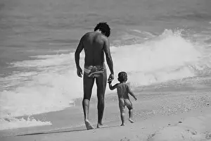 Man And Nude Son Walking On Beach