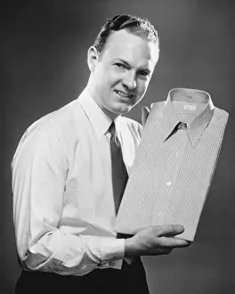 Wavy Hair Prints: Man presenting folded shirt in studio, (B&W), portrait