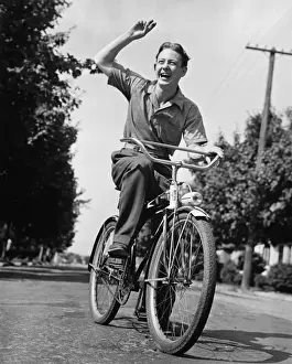 Man riding bicycle, waving, (B&W)
