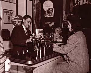 Man serving woman at soda fountain (B&W sepia tone)