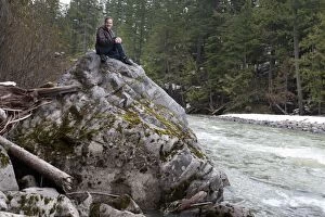 Images Dated 1st April 2011: A Man Sits On A Large Rock Elevated Above The River Flowing Below In Jasper National Park