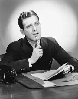 Papers Prints: Man sitting at desk, holding pencil to lip, (B&W), portrait
