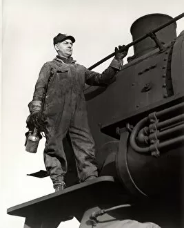 Man standing on train engine, holding oil can
