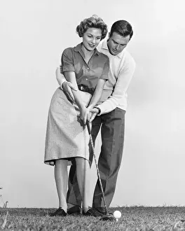 Mid Adult Couple Prints: Man teaching woman how to hit golfball