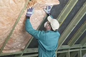 Images Dated 7th July 2004: Man wearing overalls, mask, gloves and cap, filling the space between rafters with an insulation