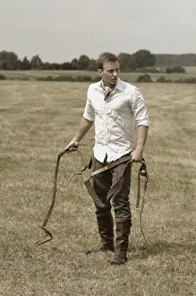Leather Gallery: Man wearing riding clothes standing in a field in summer holding a leather strap