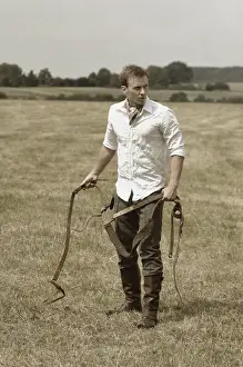 Riders Prints: Man wearing riding clothes standing in a field in summer holding a leather strap