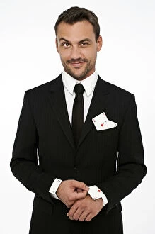 Man wearing a suit pulling an ace of diamonds out of his sleeve with other aces in his pocket