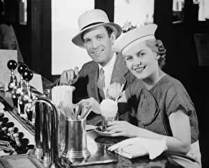 Glove Prints: Man and woman in fancy hat drinking ice cream soda (B&W), portrait