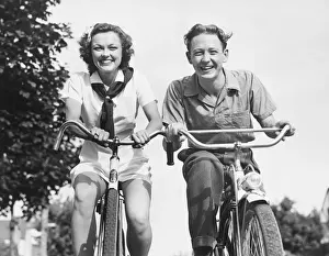 Man and woman riding bikes, (B&W), low angle view