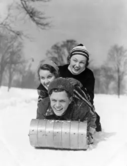 Winter Sport Prints: Man And Two Women Wearing Wool Hats And Winter Clothing Tobogganing In Snow With Tree