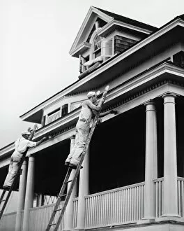 Two manual workers on ladders painting house exterior, (B&W)