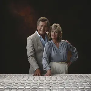 1980 Prints: Mature couple standing against black background, smiling, portrait