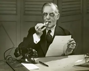 Mature man lights cigar at desk