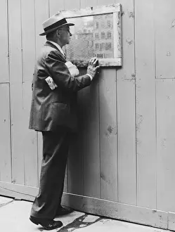Mature man looking through window in fence at construction site (B&W)