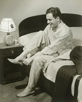Mature man sitting on bed putting on slippers, smiling